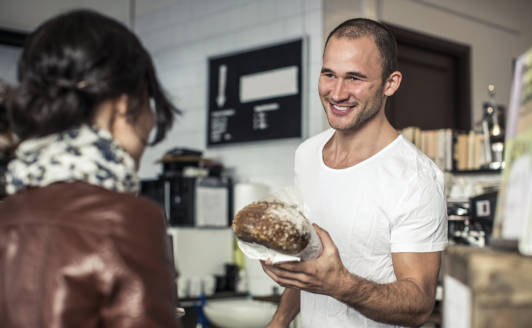Bäcker überreicht seinem Kunden ein Brot an der Bäckereien Theke